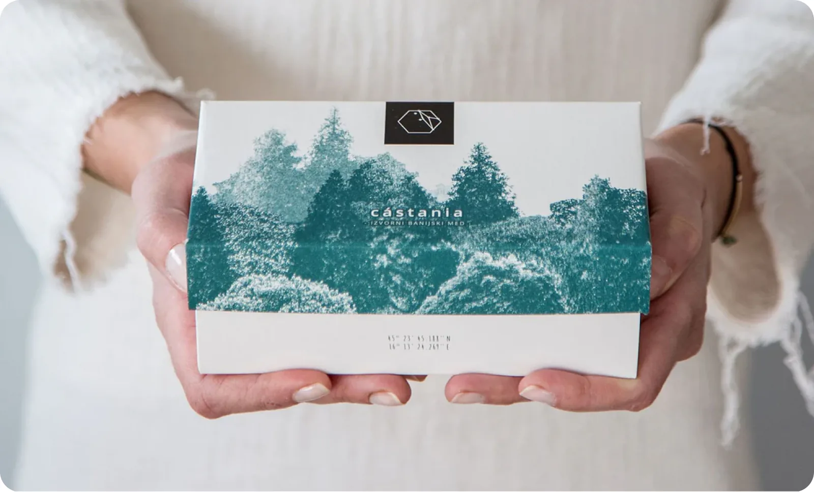 Hands holding a Castania gift box printed with a forest illustration.