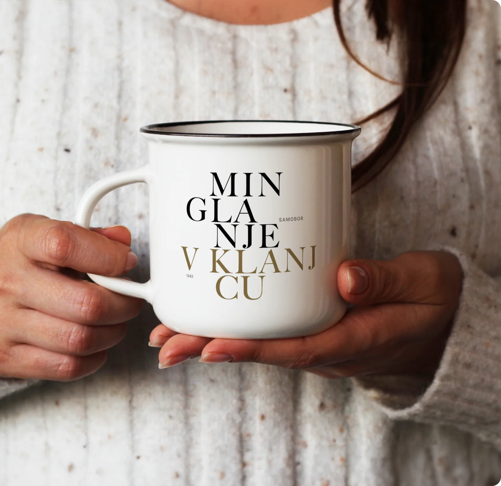 Hands cradling a white enamel mug printed with the Minglanje V Klanjcu wordmark.