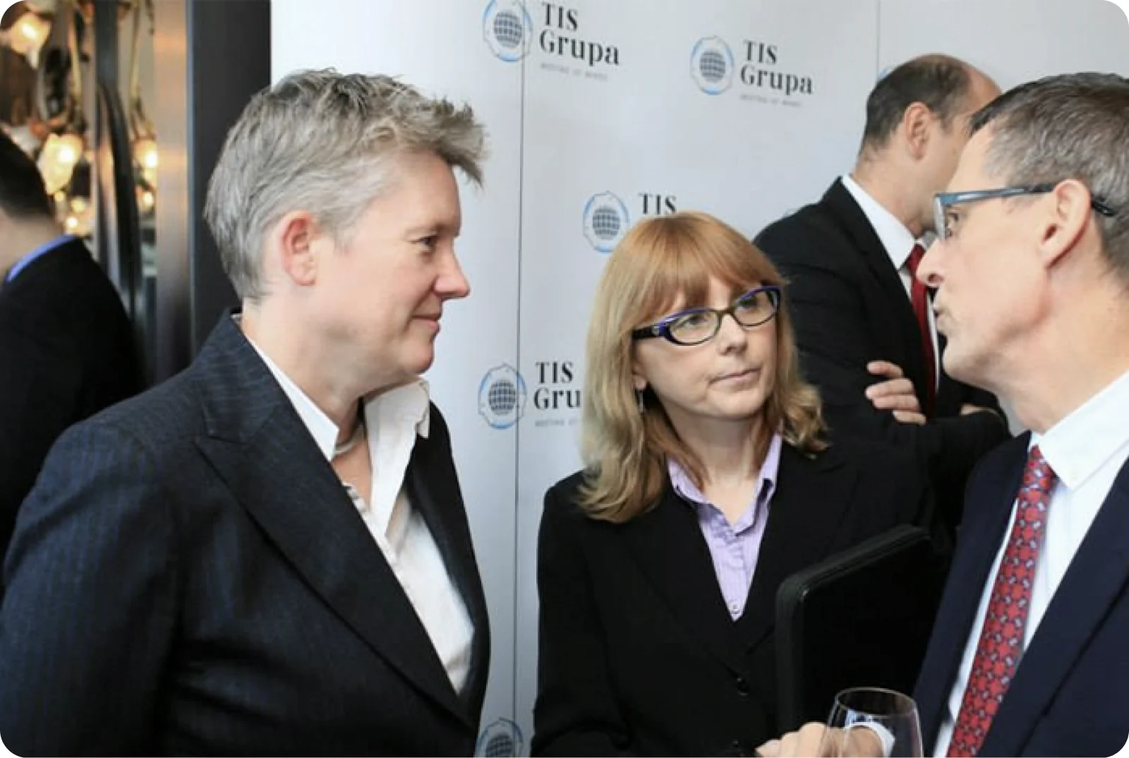 Guests in conversation in front of a TIS Grupa branded backdrop at the anniversary event.